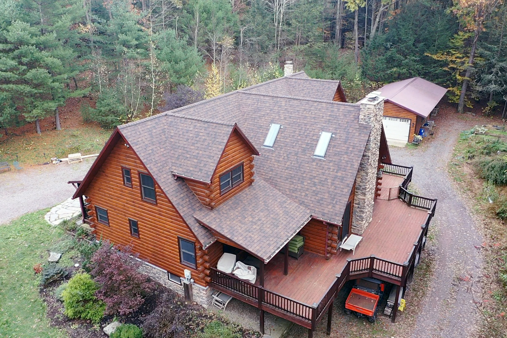 Aerial view of a completed roof on a log home surrounded by autumn forest